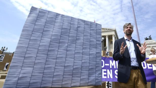 Ein Mann gestikuliert vor einem großen Plakat und dem österreichischen Parlament in Wien.