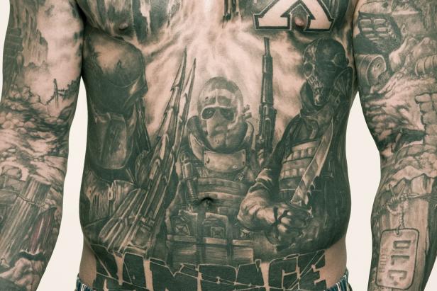 Der tätowierte Oberkörper eines Mannes zeigt eine Szene mit bewaffneten Soldaten.