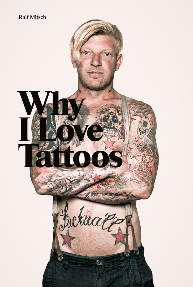 Ein Mann mit zahlreichen Tätowierungen am Oberkörper und den Armen steht mit verschränkten Armen da.