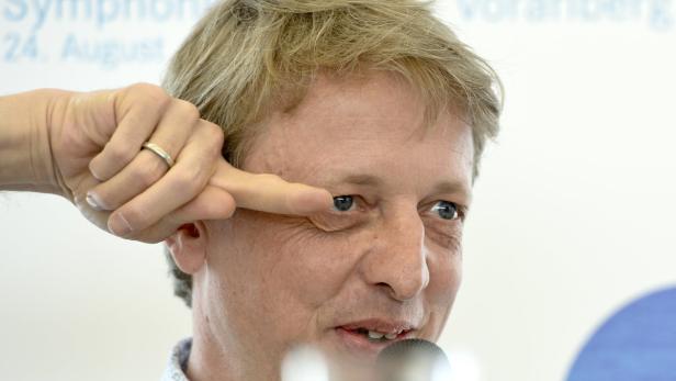 Ein Mann mit blonden Haaren gestikuliert vor einem Mikrofon.