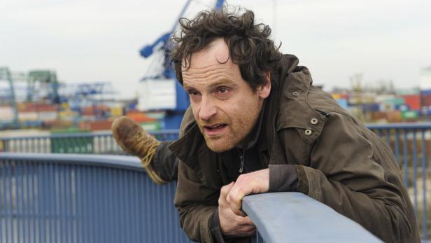 Ein Mann in Jacke klettert über ein blaues Geländer im Hafen.