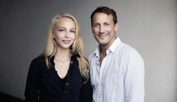 Eine blonde Frau und ein Mann lächeln in die Kamera.