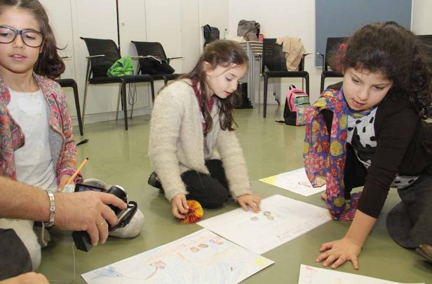 Drei Mädchen sitzen auf dem Boden und betrachten ihre Zeichnungen.