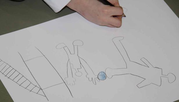 Eine Hand zeichnet eine Szene mit zwei Strichmännchen und einer Leiter auf ein Blatt Papier.