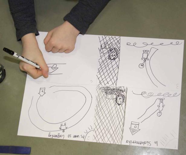 Ein Kind zeichnet mit einem Stift eine Comic-Geschichte auf ein Blatt Papier.