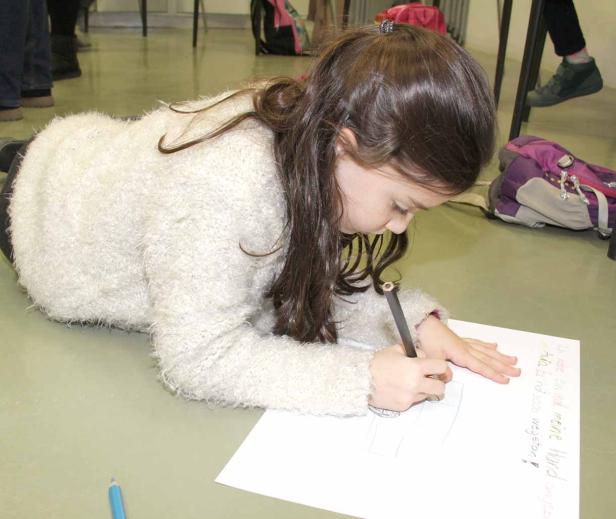 Ein Mädchen liegt auf dem Boden und zeichnet mit einem Stift auf ein Blatt Papier.