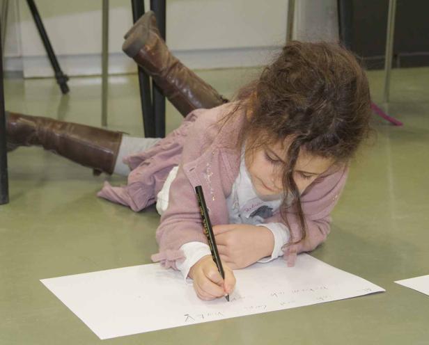 Ein Mädchen liegt auf dem Boden und schreibt auf ein Blatt Papier.