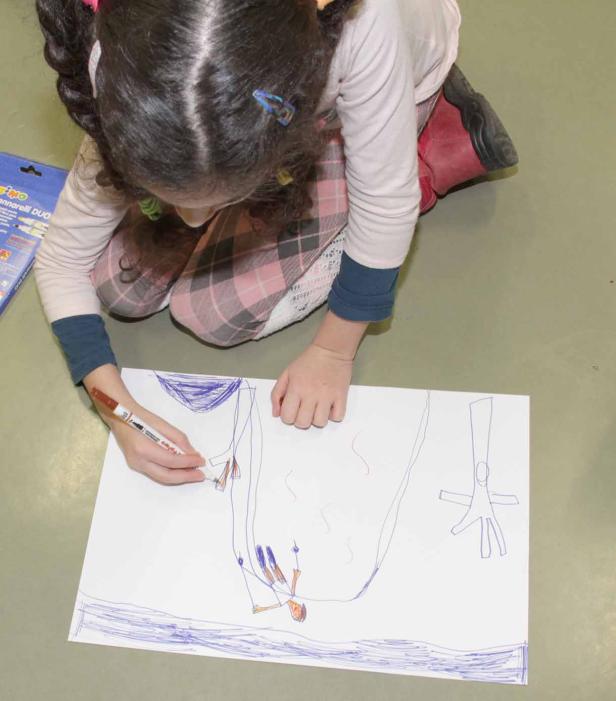 Ein Mädchen zeichnet mit einem braunen Stift ein Bild auf ein Blatt Papier.