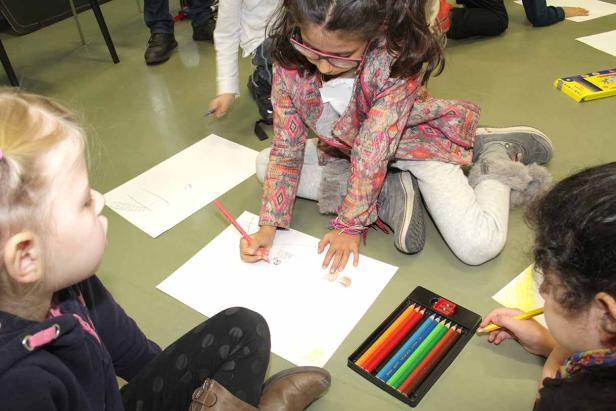 Mehrere Kinder sitzen auf dem Boden und malen mit Buntstiften auf Papier.