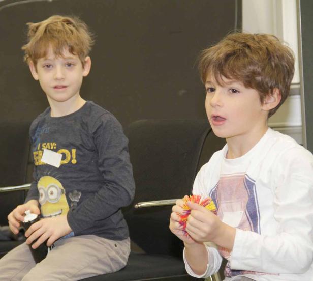Zwei Jungen sitzen auf Stühlen, einer hält eine Wasserflasche, der andere einen bunten Ball.