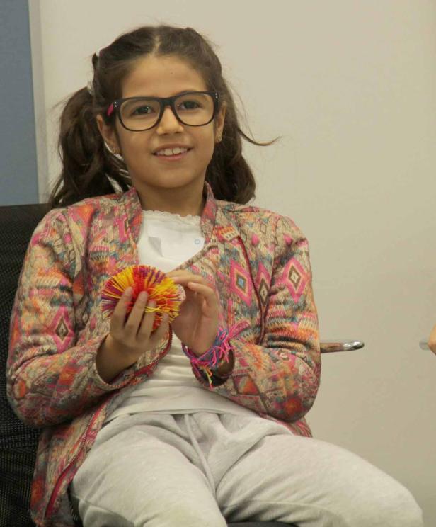 Ein junges Mädchen mit Brille sitzt und hält einen bunten Ball in den Händen.