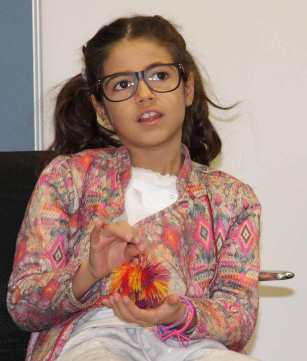 Ein junges Mädchen mit Brille hält einen bunten Bommel in den Händen.