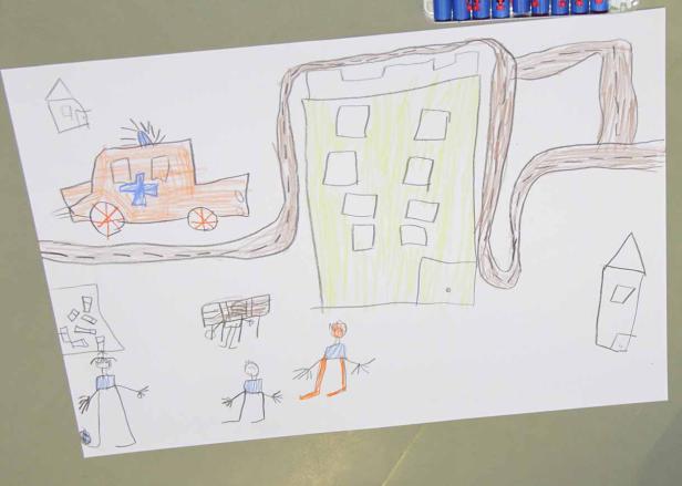 Eine Kinderzeichnung zeigt eine Stadt mit einem Krankenwagen und Menschen.