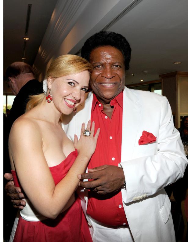 Roberto Blanco stellt neue CD vor Ein Mann in einem weißen Anzug und ein Frau in einem roten Kleid posieren lächelnd für ein Foto.
