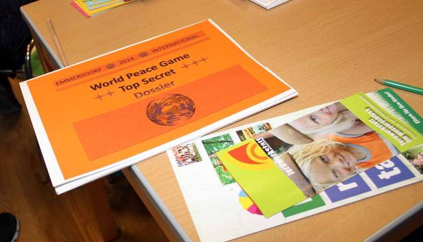 Ein Dossier des „World Peace Game“ liegt auf einem Tisch neben Flyern.