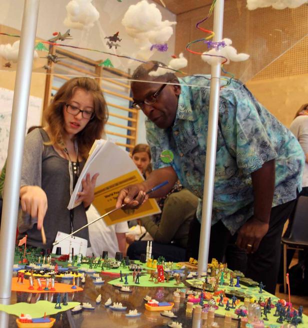 Eine Frau und ein Mann betrachten ein Modell einer Kriegslandschaft mit Figuren und Flugzeugen.