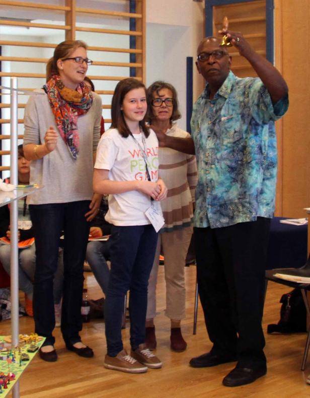 Eine Gruppe von Menschen steht in einem Raum, ein Mann läutet eine kleine Glocke.