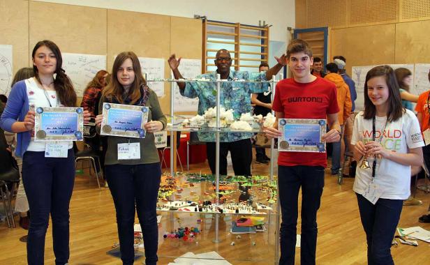 Eine Gruppe Jugendlicher hält Urkunden vor einem Regal mit einer Miniaturlandschaft.