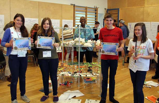 Jugendliche präsentieren Auszeichnungen für das „World Peace Game 2011“ vor einem Modell der Welt.