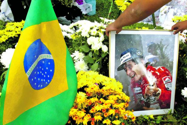 Eine brasilianische Flagge und ein gerahmtes Foto von Ayrton Senna, umgeben von Blumen.