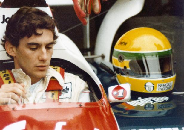 Ayrton Senna sitzt in seinem Rennwagen, neben ihm sein gelber Helm.