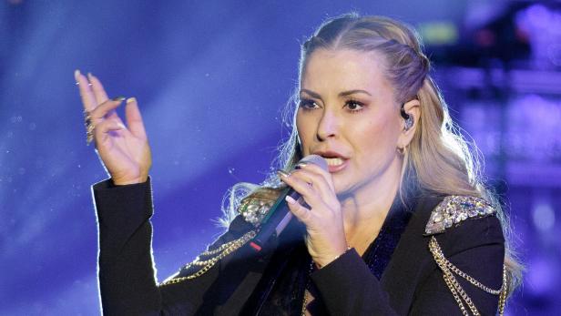 Eine Frau mit blonden Haaren singt in ein Mikrofon auf einer Bühne.