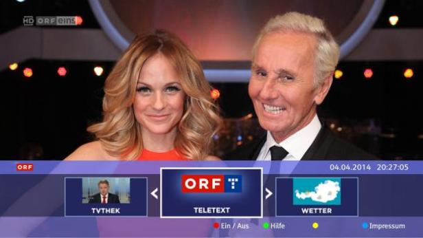 Ein Mann und eine Frau posieren vor dem Bildschirm des österreichischen Rundfunks (ORF).