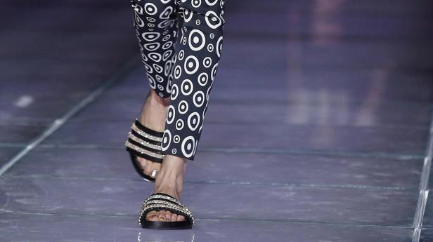 Nahaufnahme von Füßen in gemusterten Hosen und verzierten Sandalen.