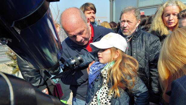 Ein Mann hilft einem Mädchen, durch ein Teleskop zu schauen.