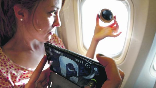 Eine Frau macht im Flugzeug ein Foto von einem Objekt vor dem Fenster.