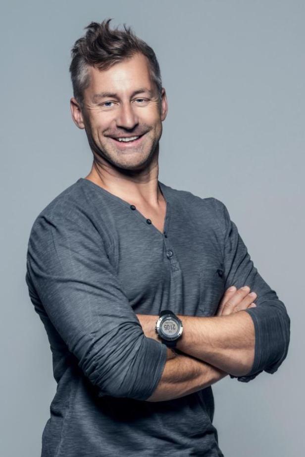 Ein Mann mit verschränkten Armen und einer Uhr lächelt in die Kamera.