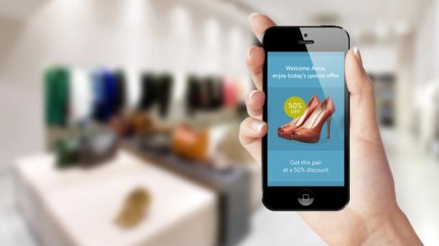 Eine Hand hält ein Smartphone mit einer Werbeaktion für Schuhe mit 50 % Rabatt in einem Geschäft.