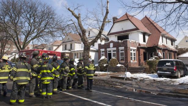 Eine Gruppe Feuerwehrleute steht vor einem Haus mit Brandschaden.