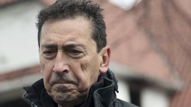 Ein Mann mit dunklen Haaren und einer dunklen Jacke blickt nachdenklich nach unten.