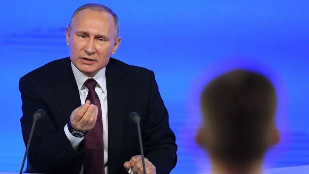 Wladimir Putin gestikuliert während einer Pressekonferenz vor einem blauen Hintergrund.