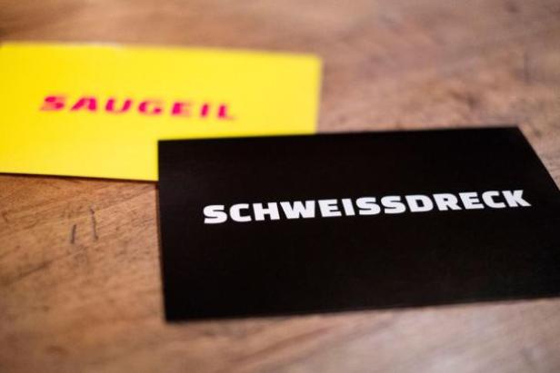 Zwei Karten mit den Aufschriften „Saugeil“ und „Schweissdreck“ liegen auf einem Tisch.