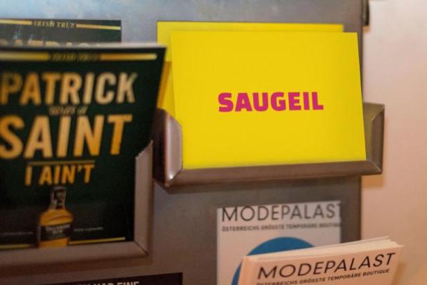 Ein gelber Zettel mit der Aufschrift „SAUGEIL“ in einem Regal mit Flyern und Broschüren.
