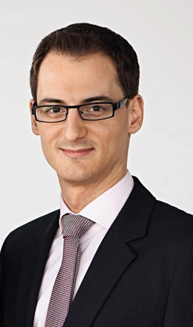 Ein Mann mit Brille, Anzug und Krawatte lächelt in die Kamera.