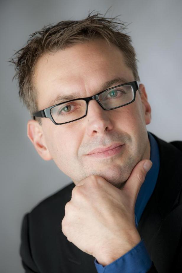 Ein Mann mit Brille und Anzug hält seine Hand ans Kinn.