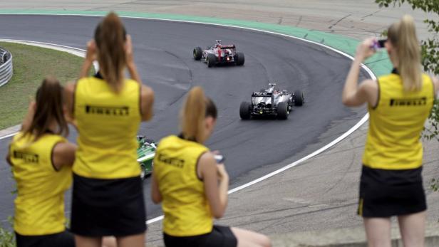 Zuschauerinnen beobachten zwei Formel-1-Rennwagen auf einer Rennstrecke.