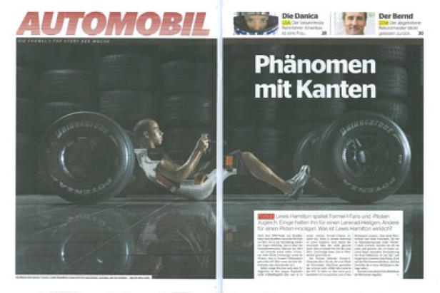 Lewis Hamilton sitzt zwischen Reifen und spielt mit einem Lenkrad.