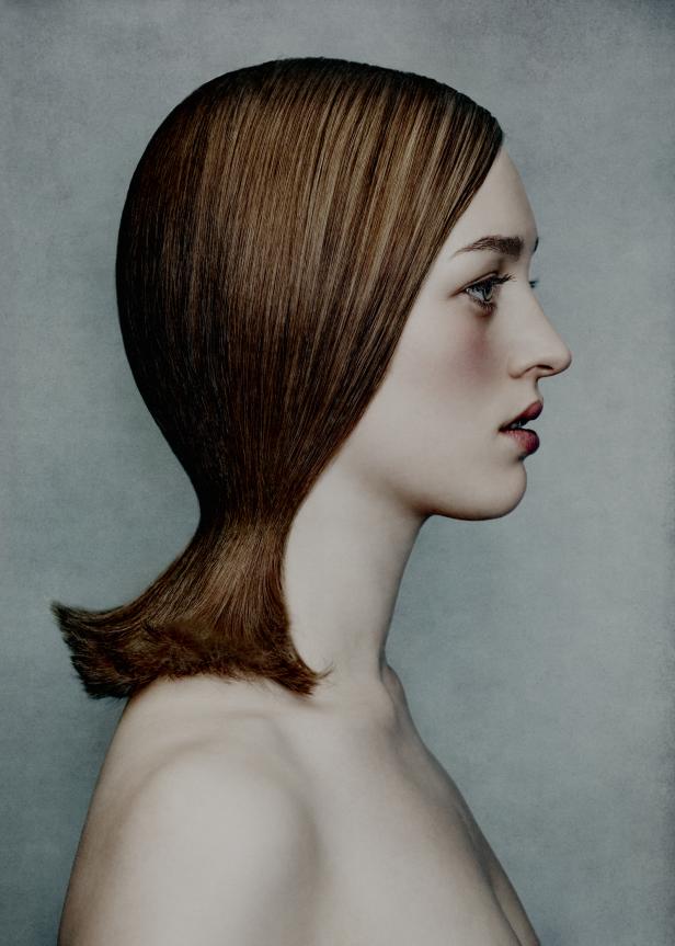 Das Profil einer Frau mit kinnlangem, glattem Haar vor einem grauen Hintergrund.