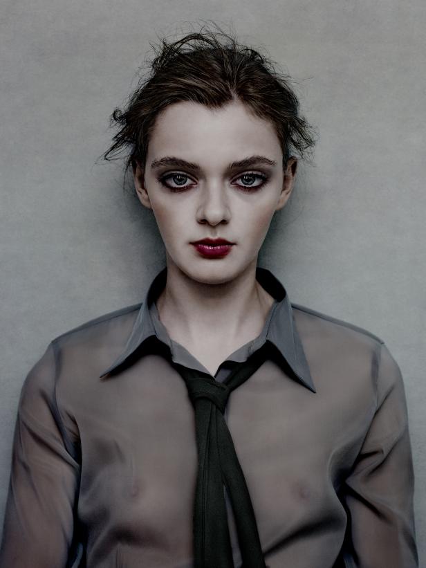 Eine Frau mit dunklem Haar und dunklem Lippenstift trägt eine durchscheinende Bluse mit Krawatte.