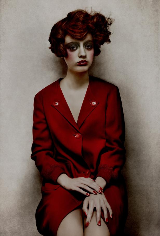 Eine Frau mit rotem Haar und starkem Make-up trägt ein rotes Kleid.
