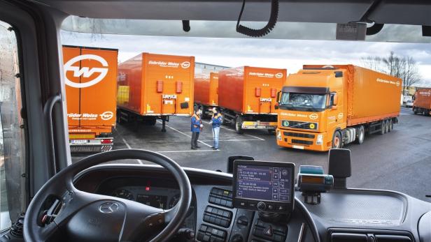 Blick aus dem Führerhaus eines Lkw auf orangefarbene Gebrüder Weiss-Lkw auf einem Parkplatz.