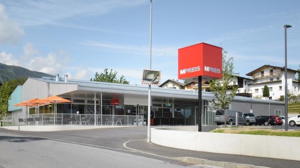 Ein MPreis-Supermarkt mit Parkplatz und Café im Freien an einem sonnigen Tag.