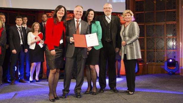 Eine Gruppe von Personen posiert auf einer Bühne mit einer Urkunde.