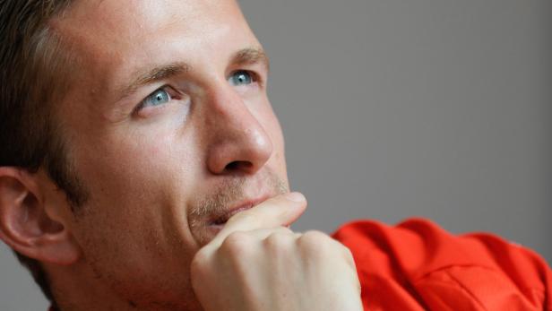 Ein Mann mit hellblauen Augen denkt nach, den Finger an die Lippe gelegt.