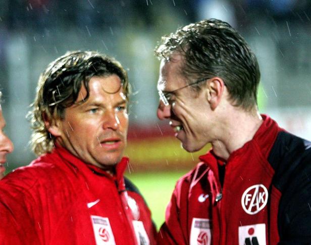 Zwei Männer in roten Jacken stehen im Regen und unterhalten sich.