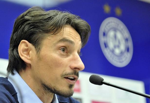 Ein Mann spricht in ein Mikrofon vor einem blauen Hintergrund mit einem Logo.